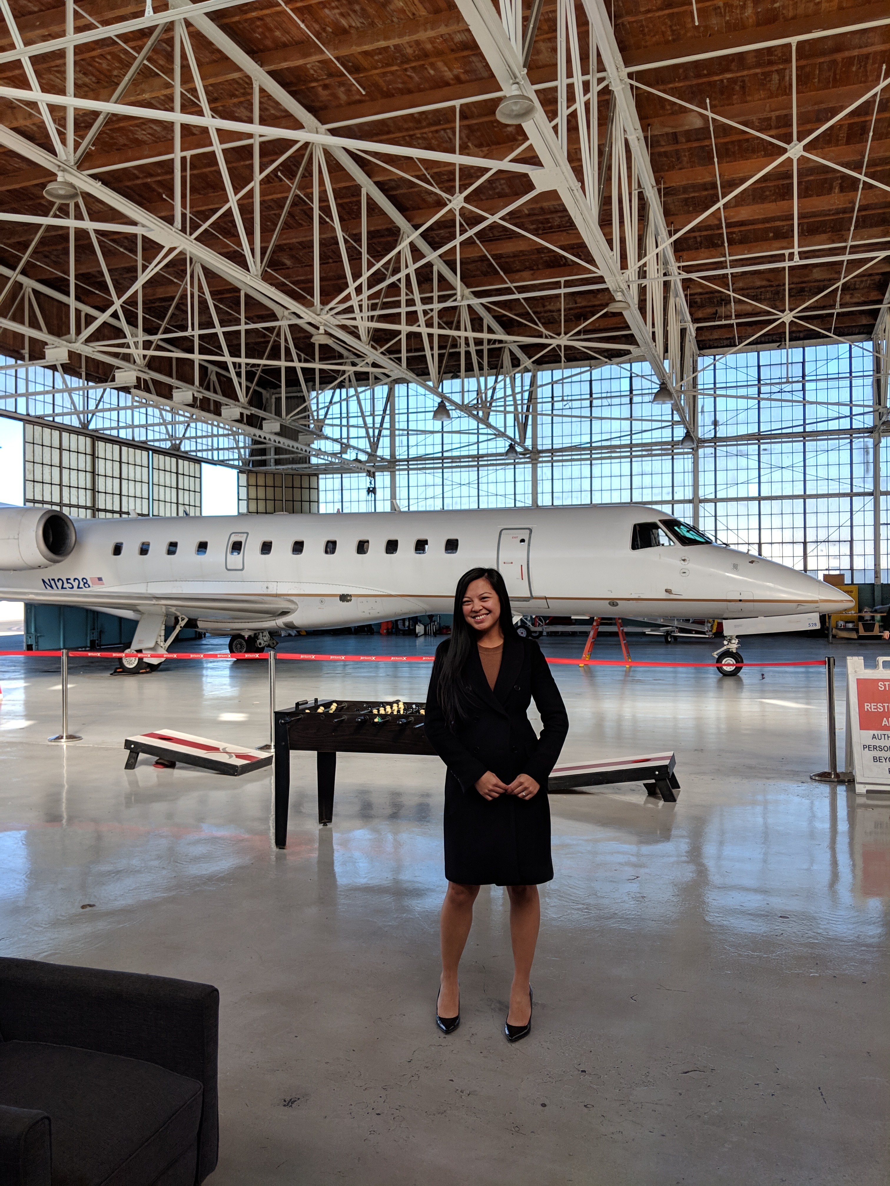 Adrienne flying to another tech conference, pictured in a hangar with a jet in the background