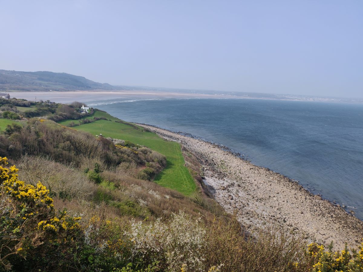 the view from a hillside overlooking the beach and sea on the Anglesey Coastal Path