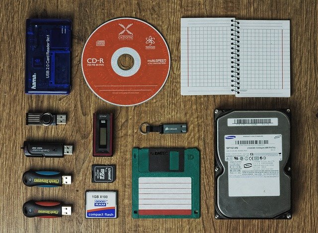 An assortment of computer storage devices including multiple thumb drives, SD Card, Floppy Disk, CD, and hard disk drive 