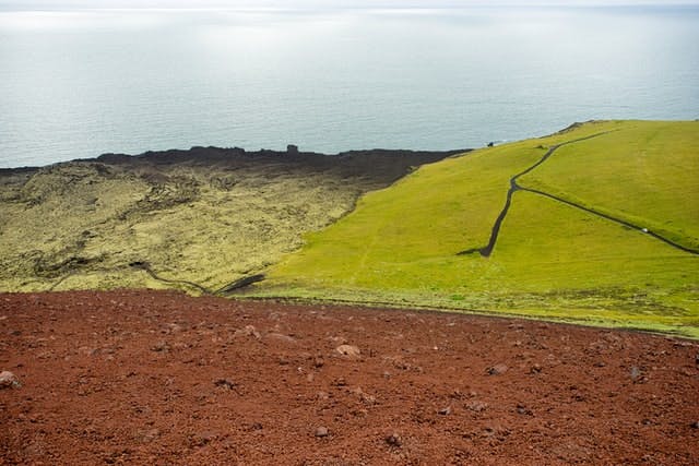 A view of the ocean from the top of a hill with different types of soils.