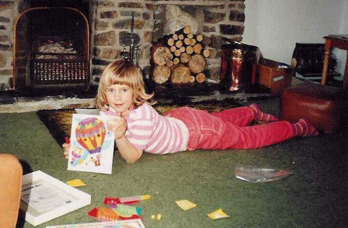 Young Sara lying on the floor with a piece of art in her hands