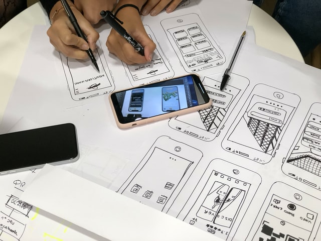 people working on a wireframe with a phone, pens and paper