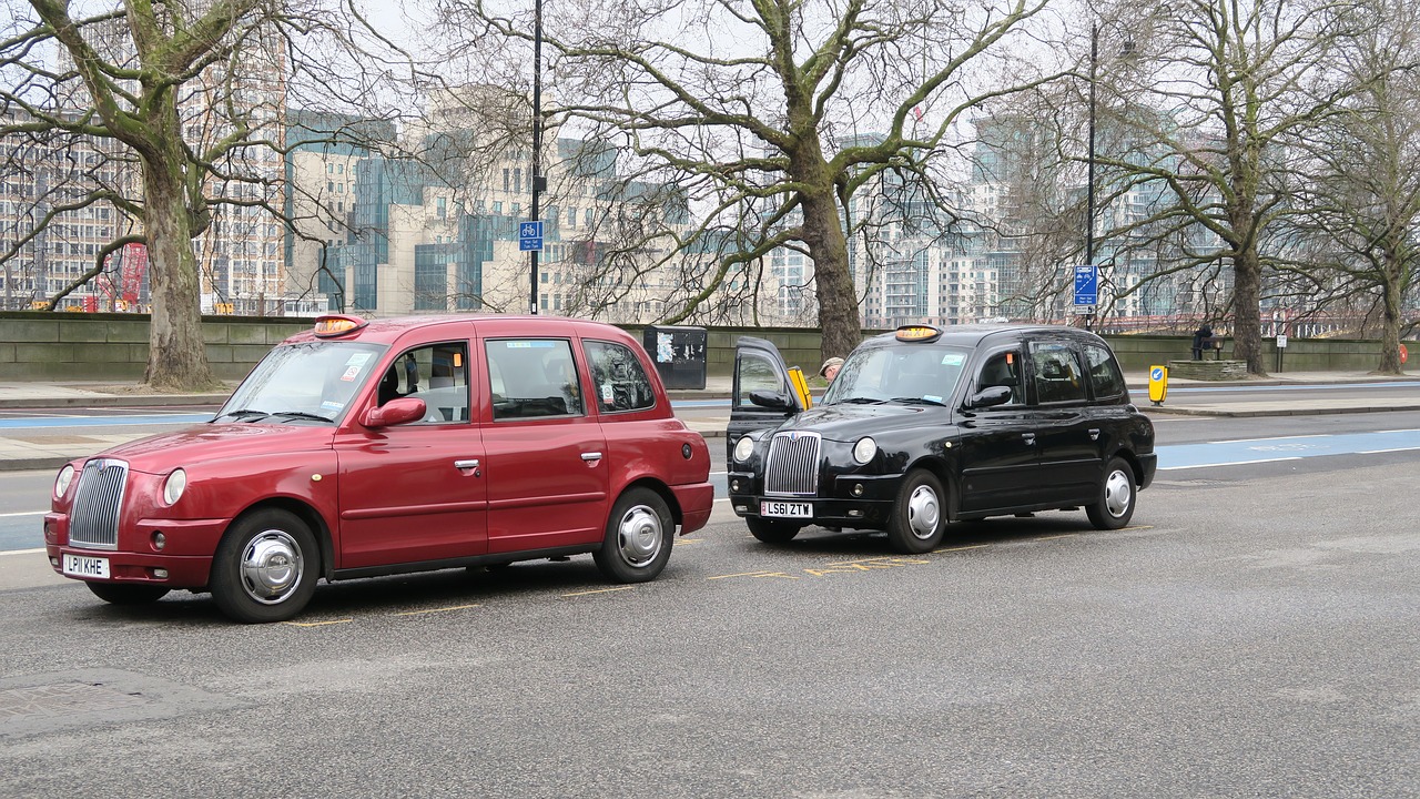 A picture of a red, slightly bigger taxi cab in front of a black, smaller taxi cab