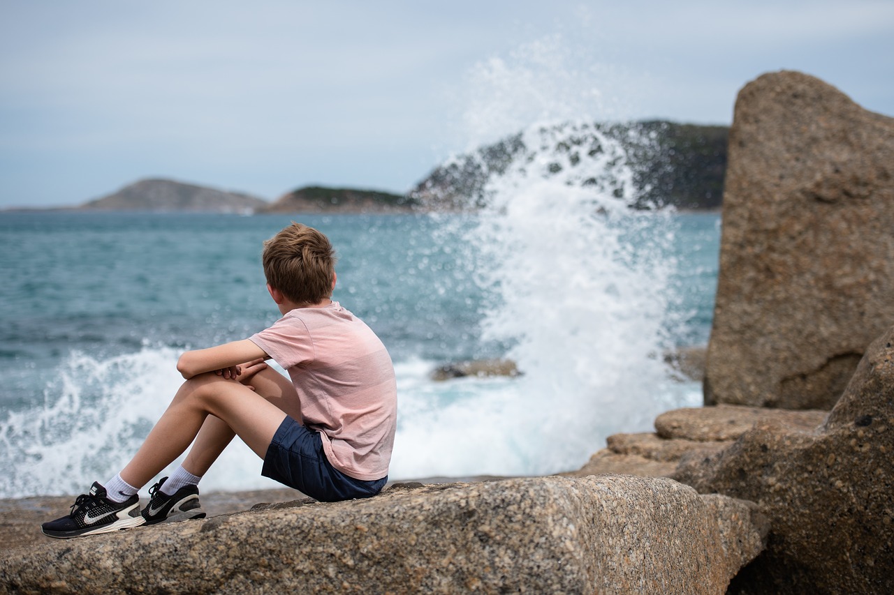A picture of a boy sitting on rocky shore by the ocean