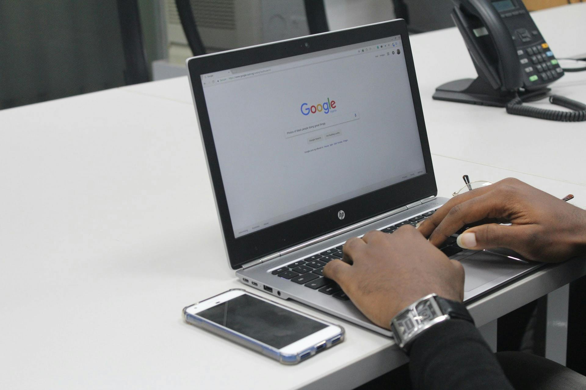 A person making a Google search on a laptop computer at a desk.