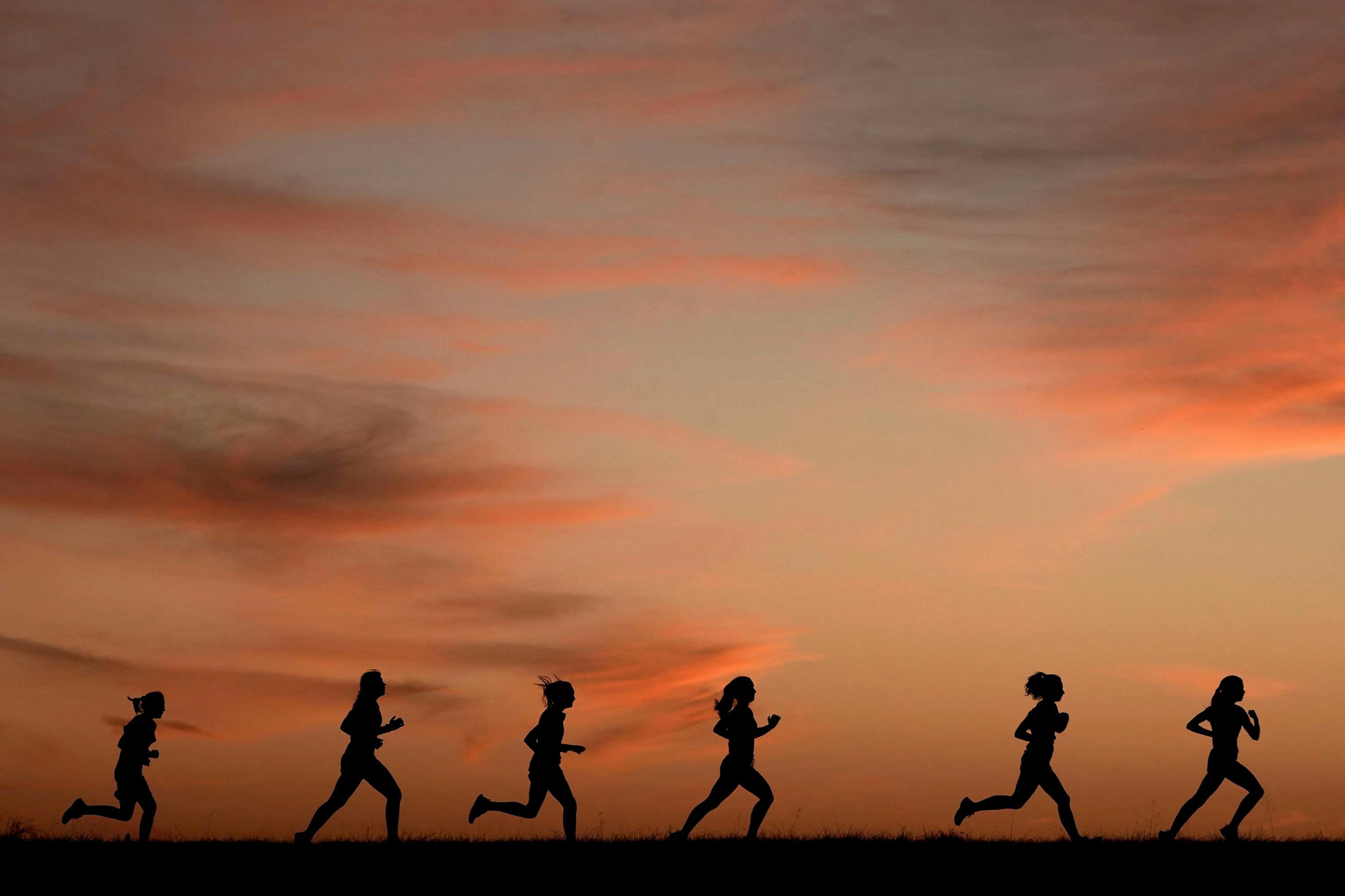 A group of individuals engaged in a lively run, each wearing athletic attire and running shoes, displaying energetic and determined expressions on their faces as they move forward with determination.