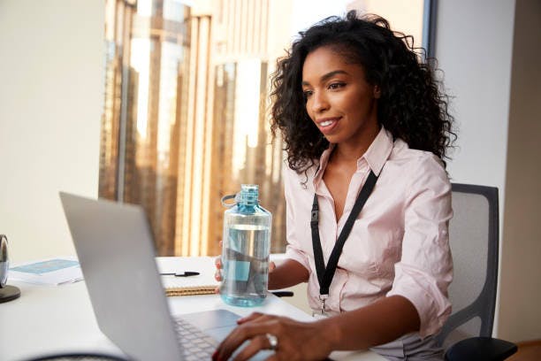 A clear bottle filled with refreshing water, taking by some one pressing her laptop