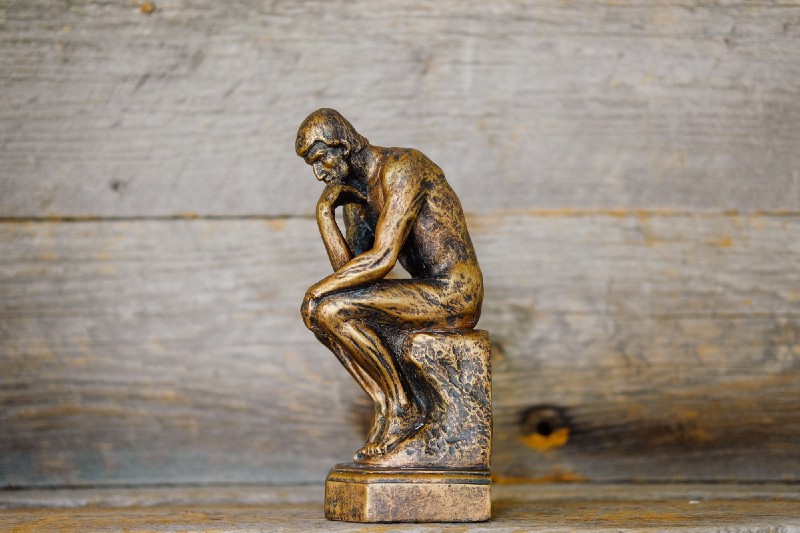 a miniature version of the thinking man statue in the foreground and worn wood in the background