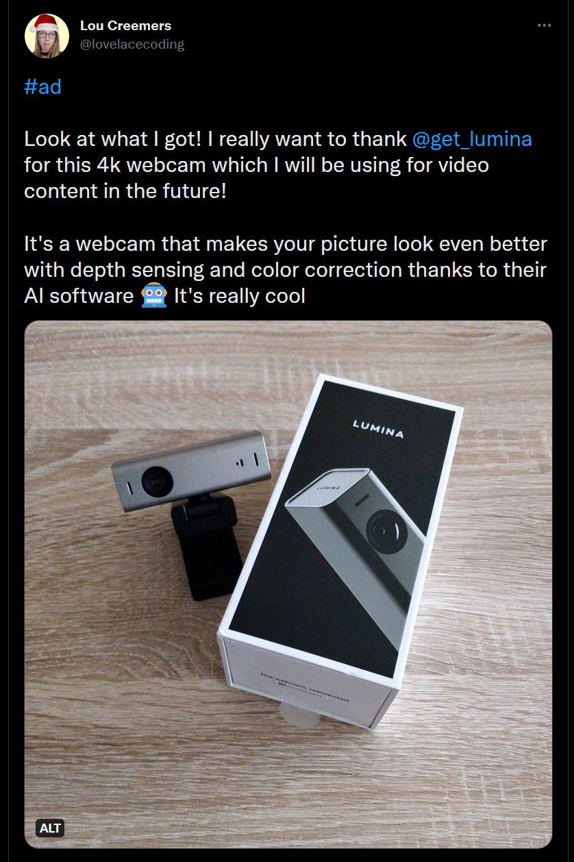 Ad tweet by Lou Creemers for Lumina. There's a picture of the box of a gray webcam, with the actual webcam next to it. The text says 'Look at what I got! It's a webcam from Lumina that makes your picture look even beter with depth sensing and color correction thanks to their AI software. It's really cool,'