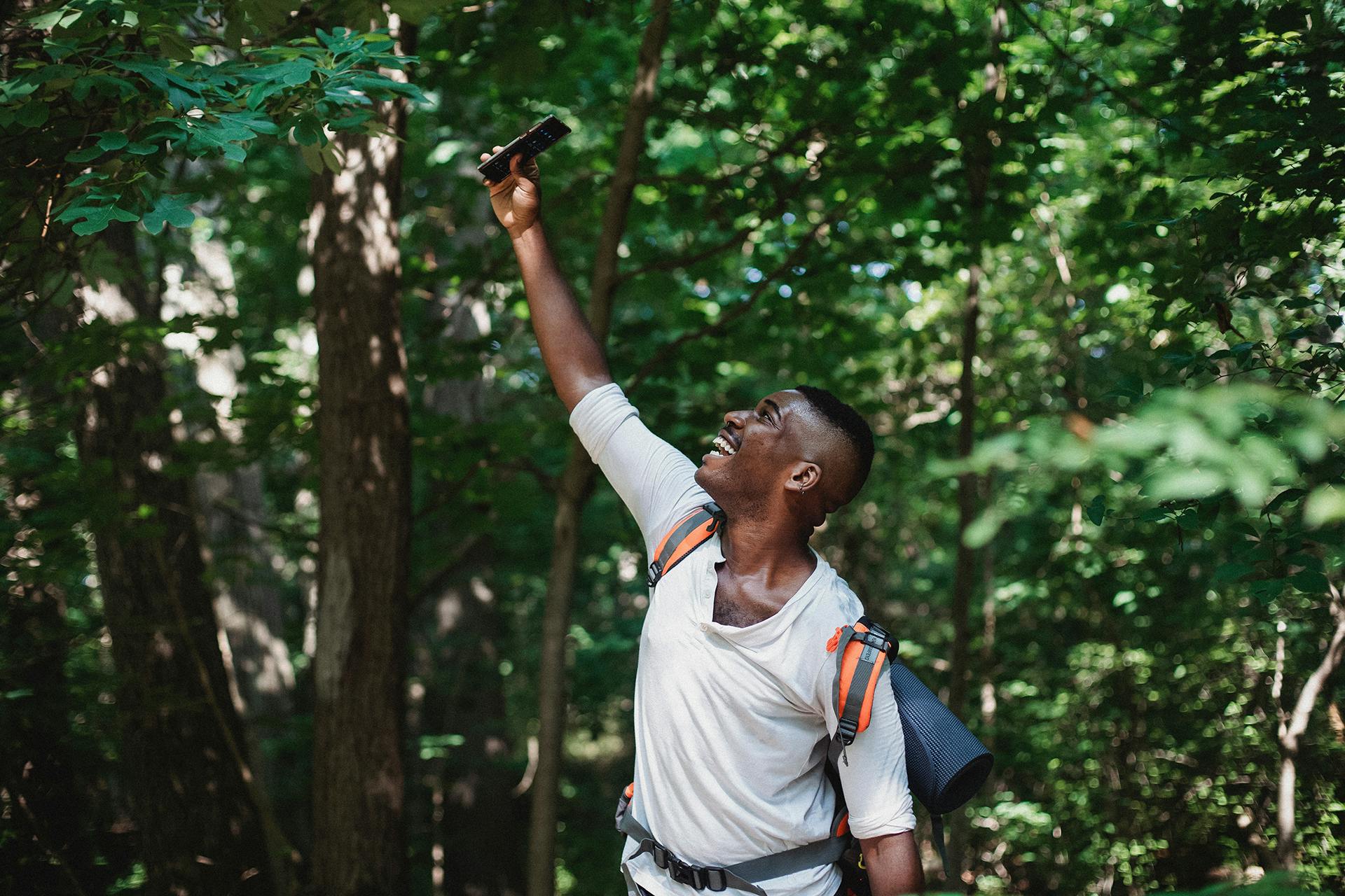 A man holds his mobile phone up in the woods, searching for internet connection
