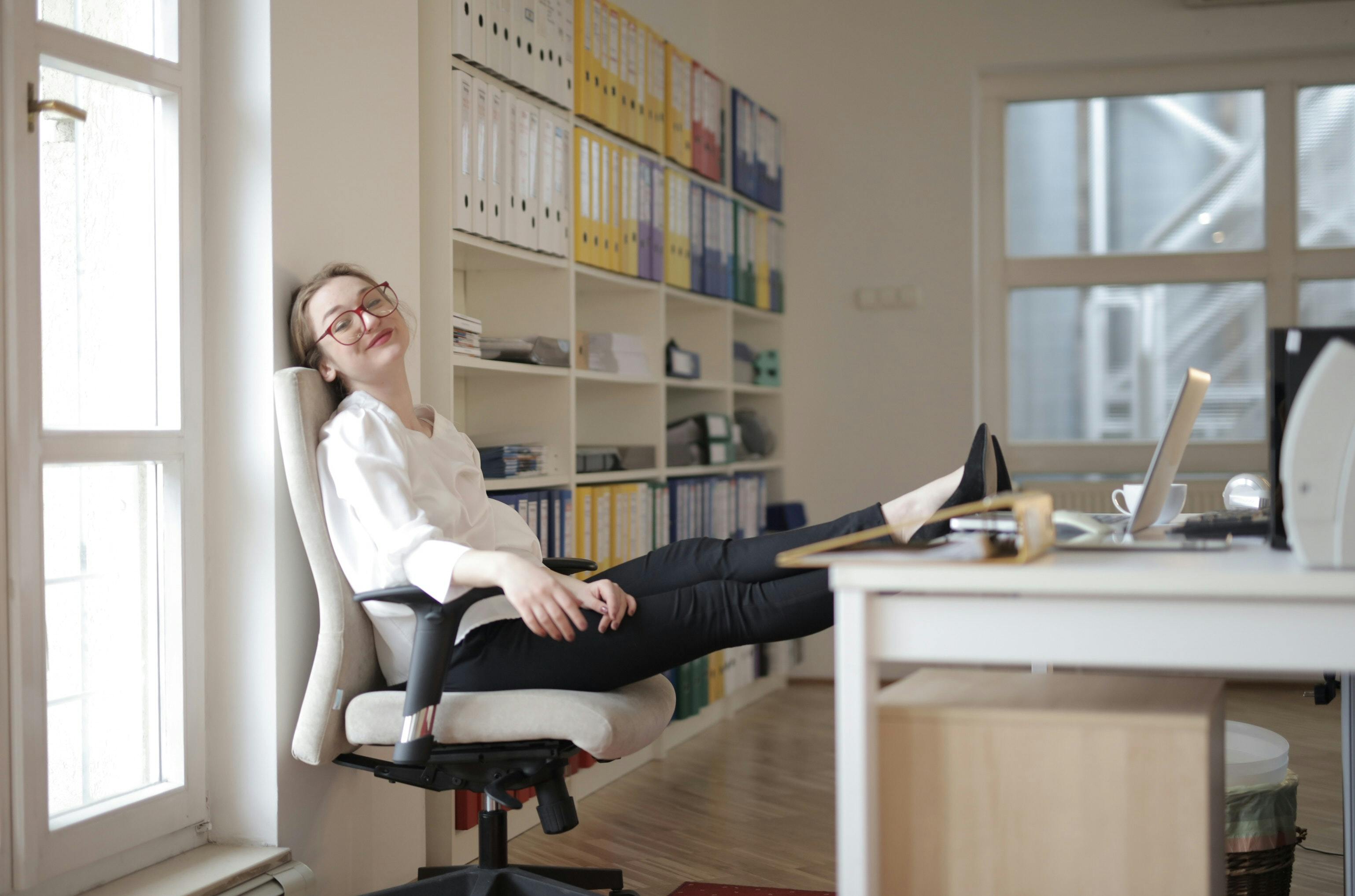 A developer sits at her desk with her legs up on the table, with a relaxed look on her face.