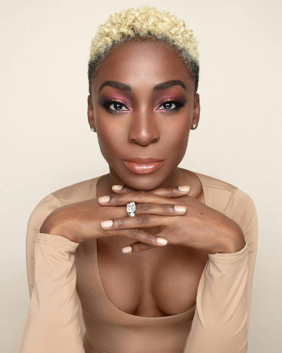 Angelica Ross is a dark-skinned Black woman with a blonde buzzcut with piercing eyes and a soft smile