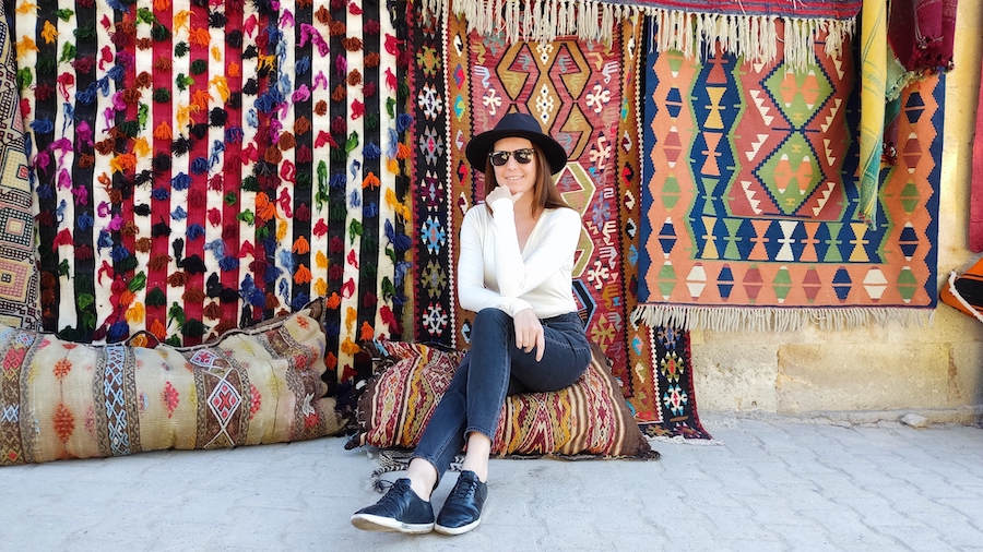 kobieta siedzi przy cianie kolorowych dywanw