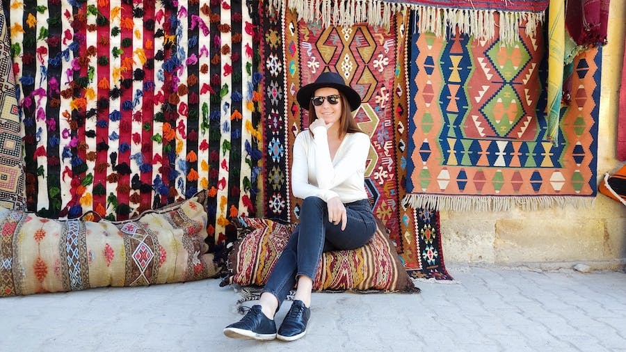 kobieta siedzi przy ścianie kolorowych dywanów