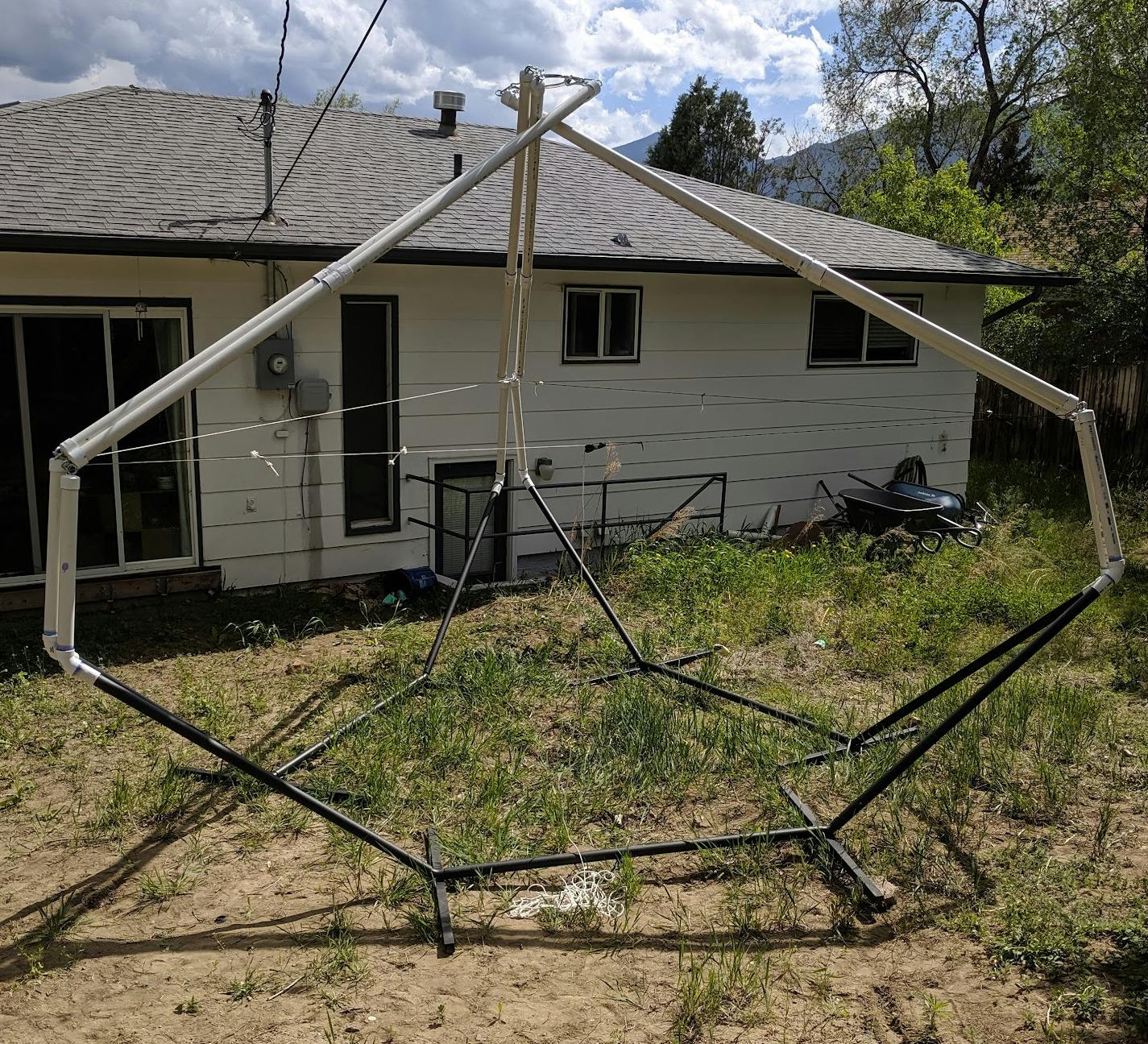 Three hammock stands in a triangle, with PVC pipes sprouting from their ends and coming back together in the center to form a roof.  A rope stretches around the waist of the structure to prevent it from flattening like a pancake.