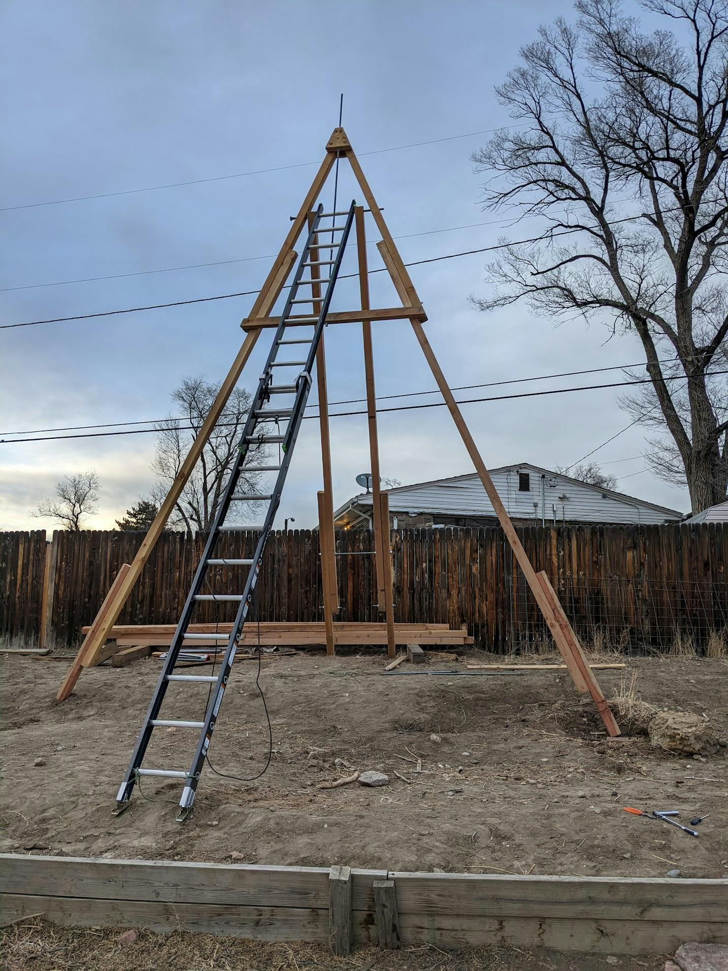 A wooden pyramid with a ladder as one edge, taller than my neighbor's house behind it.