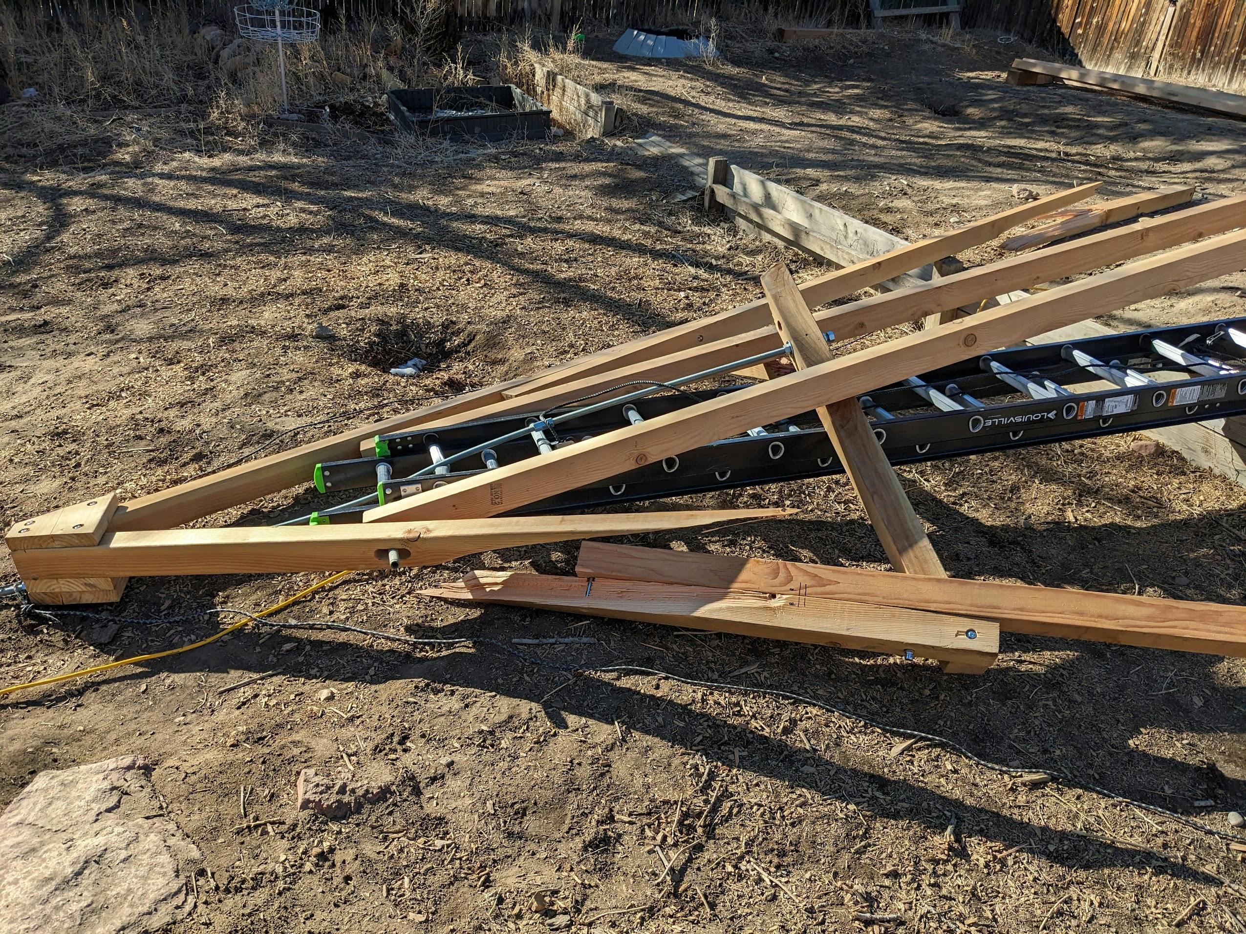 A pile of ladder and lumber.  The vertical threaded rod has bent a groove into the top rungs of the ladder.  Several beams are splintered.  Some lumber might be salvageable. 