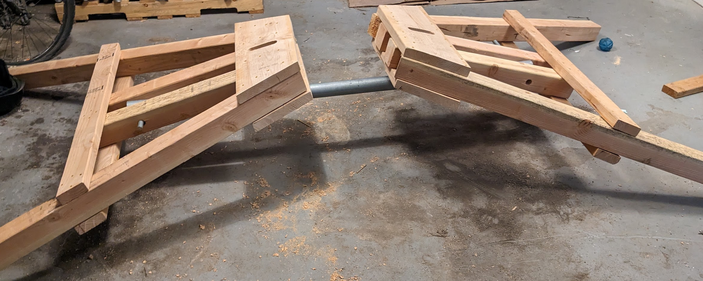 Two A-frames, facing each other, tilted with their apexes facing each other and their feet away from each other.  they are joined by a steel pipe.