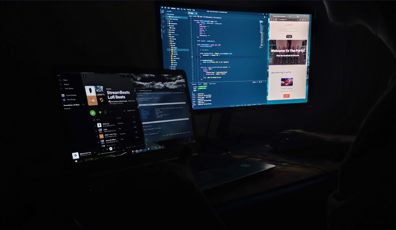 A photo of me looking at my laptop with VSCode and live preview on one monitor and Spotify and a backend server running on another screen.