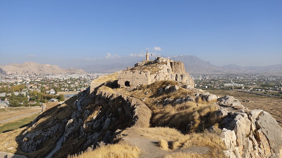 forteca z widocznym minaretem położona na skalnym wzniesieniu, w tle miasto a dalej góry