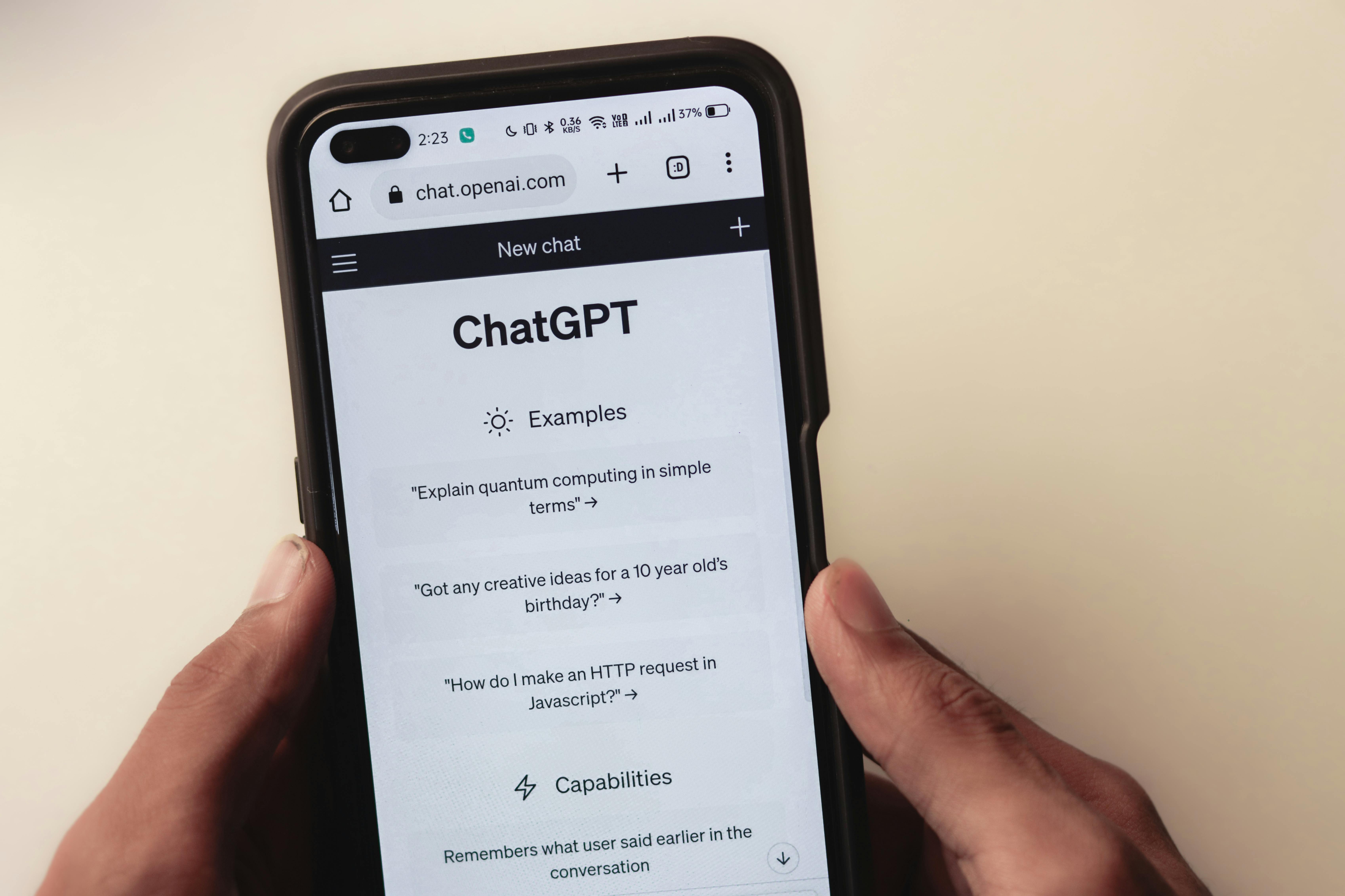 Two hands holding a phone. On the phone screen you can see that the ChatGPT website is open.