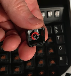 red, silicone o-ring on the bottom of a key held above a keyboard that has keys missing