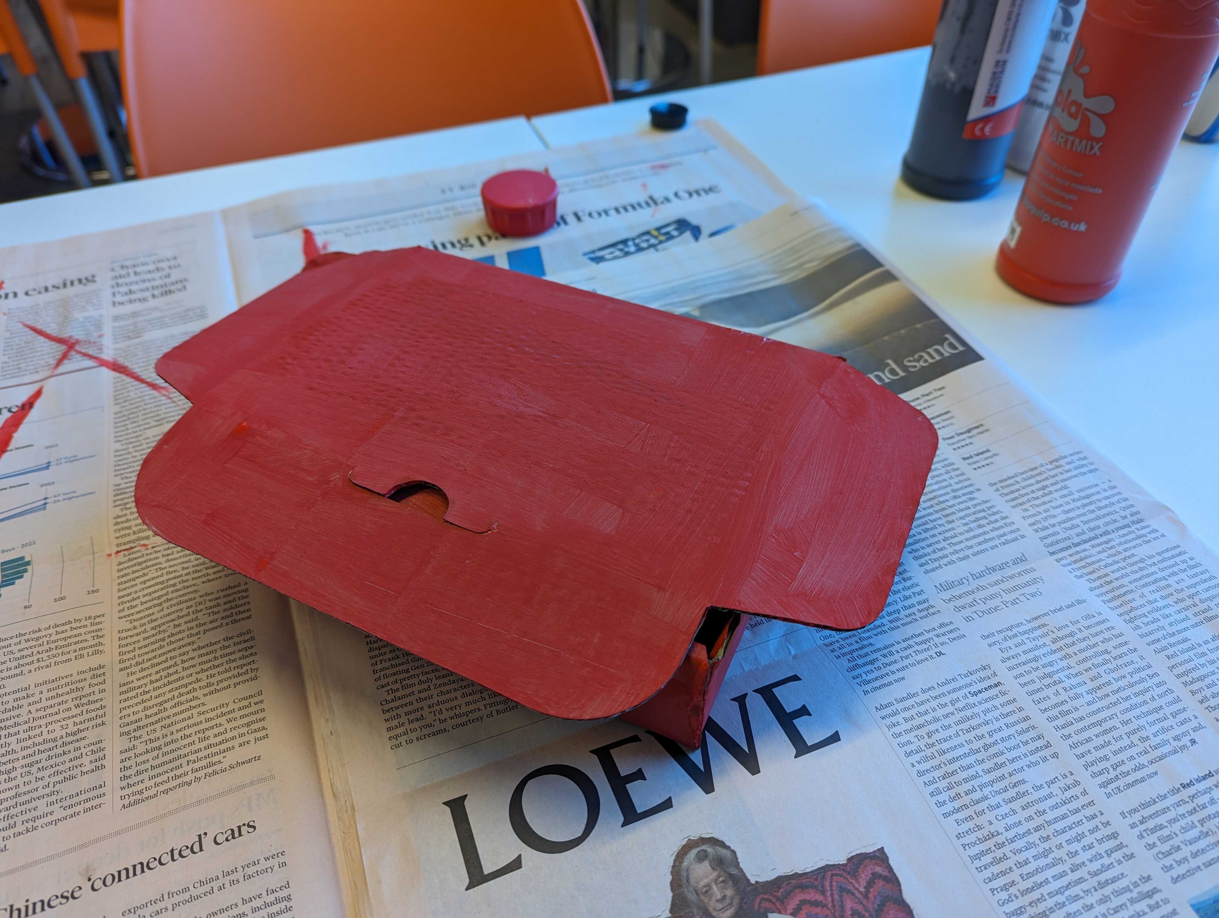 A rubbish looking cardboard box painted red on some newspaper