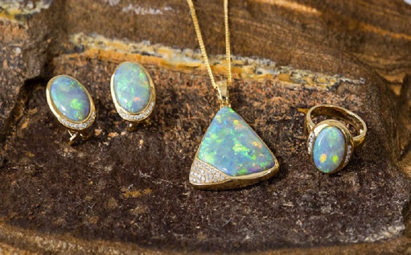 A close-up photo of opal jewelry, including a necklace, earrings, and ring, displayed on a natural rock.