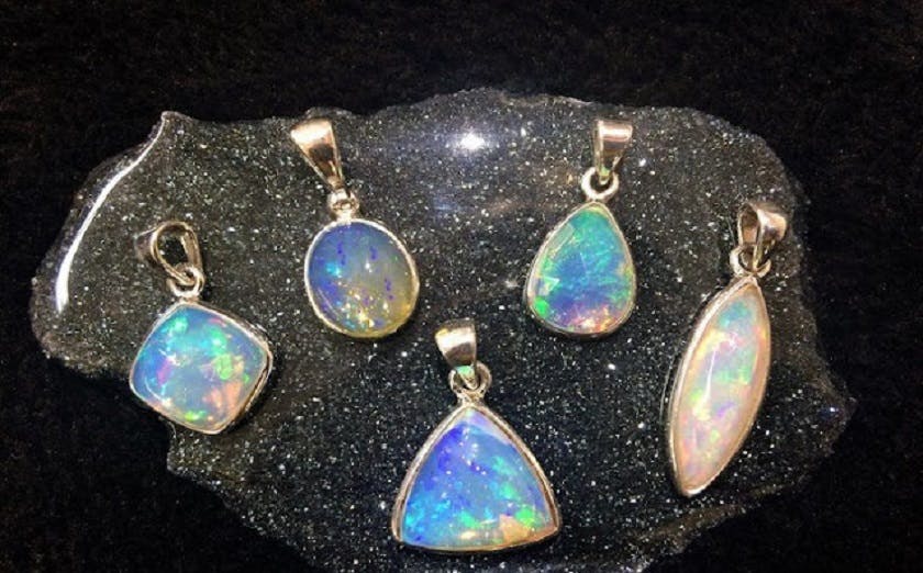 A group of opal pendants in various shapes and sizes displayed on a natural rock.