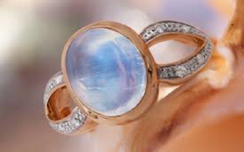 Close-up of a gold ring with a blue moonstone in the center. The ring is set on a white seashell.