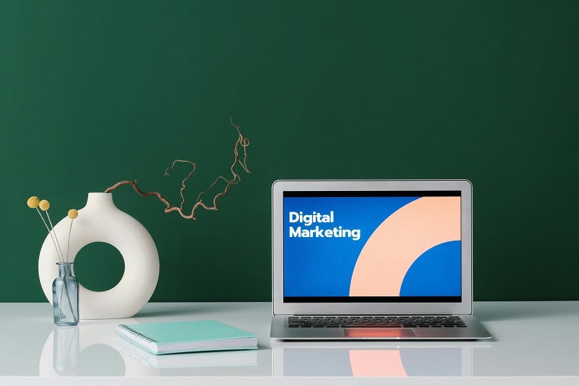 A laptop computer on a desk with a vase of flowers. The laptop screen shows text that says "Digital Marketing".