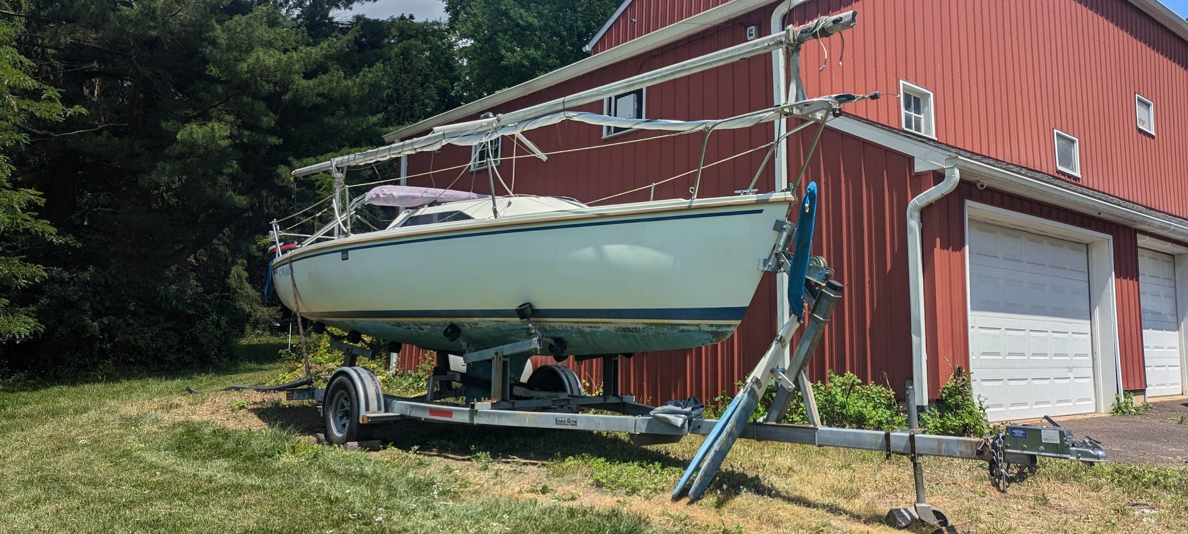 Sailboat on a trailer in front of a red barn.