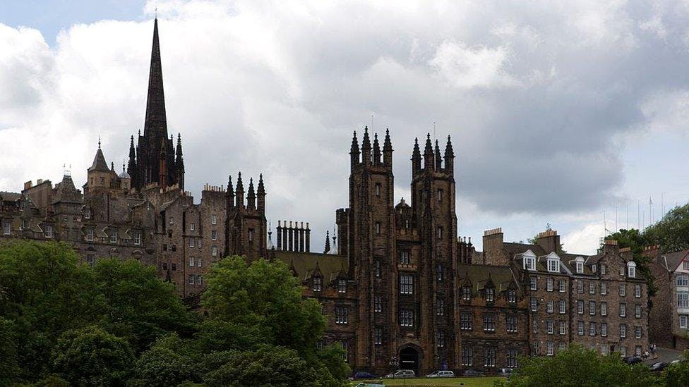 A historical, Gothic-style building with multiple spires and stone architecture, surrounded by trees under a cloudy sky. Best place for international student.