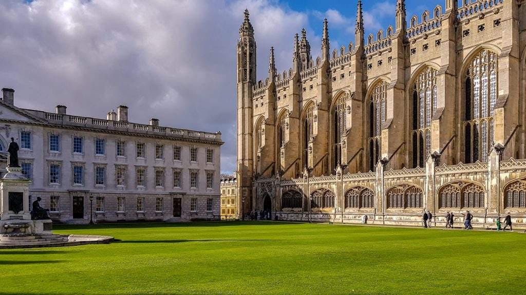 Historic building with Gothic architecture and large windows, adjacent to a manicured green lawn and a statue under a cloudy sky. Best place for international student.