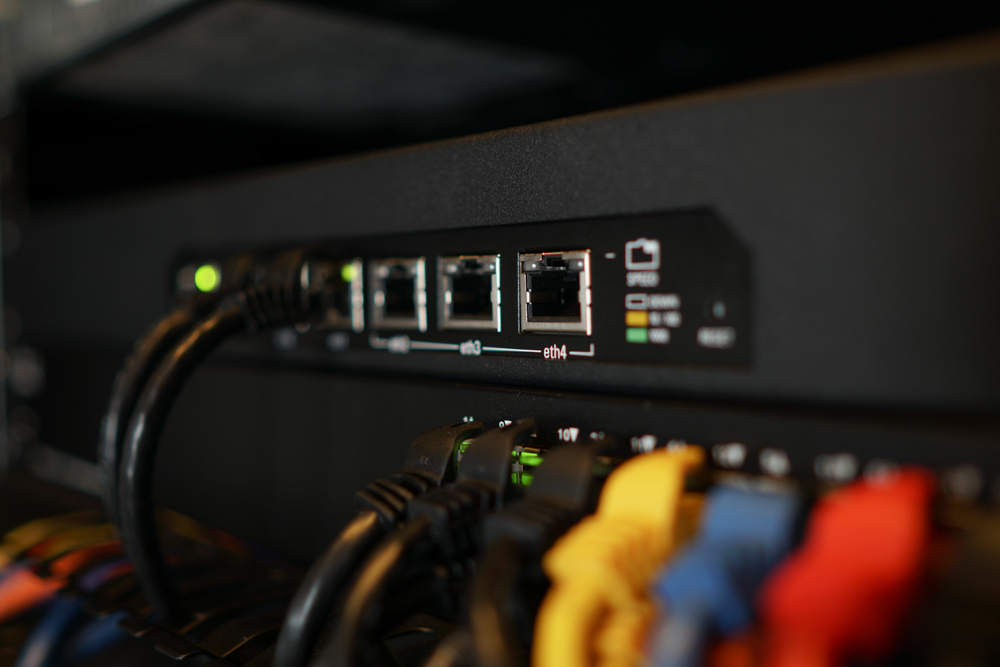 Close-up of an Ethernet switch with multiple network cables plugged into various ports, with indicator lights glowing.