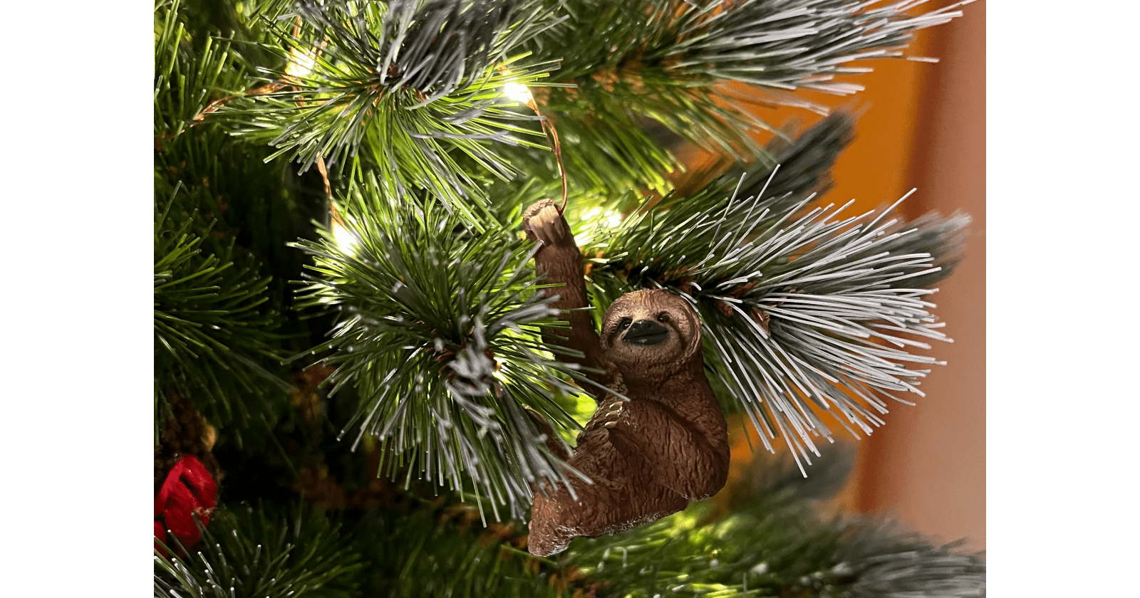 A little cute sloth ornament hanging on a Christmas tree branch with twinkling lights and celebrating its achievements.