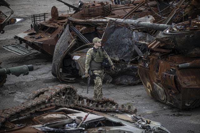 A Ukrainian soldier walking among several burned remains of armored vehicles.