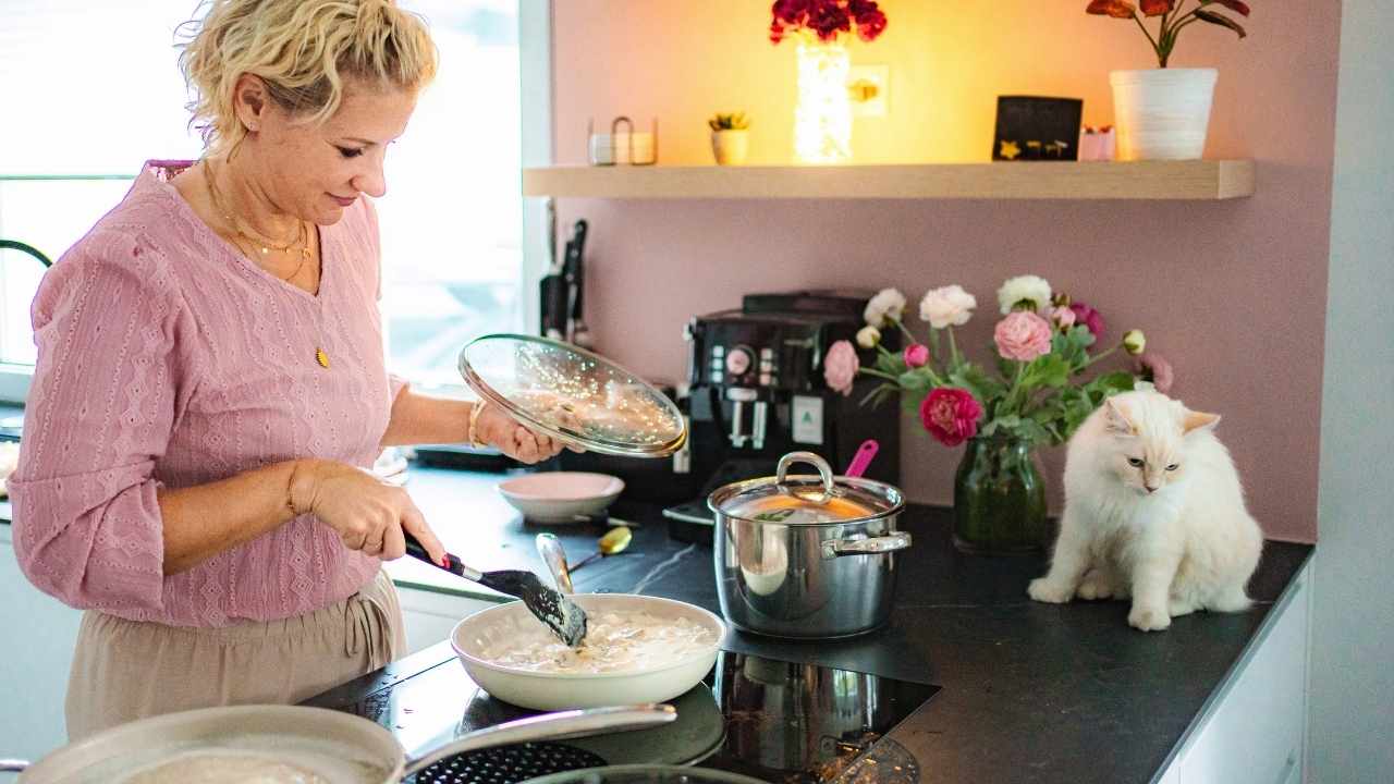 kadın ocakta yemek yapıyor ve kedi izliyor