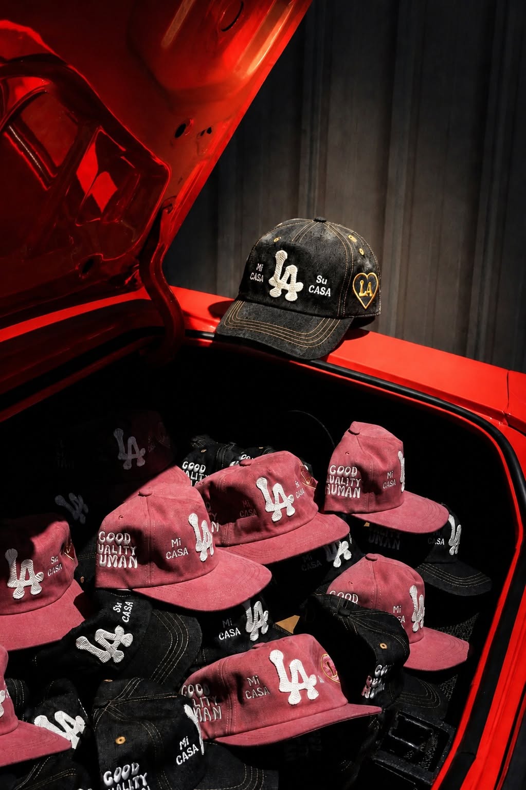 Man wearing a Good Quality Human trucker hat and Easyriders tee, sitting on a red vintage car on a Los Angeles street