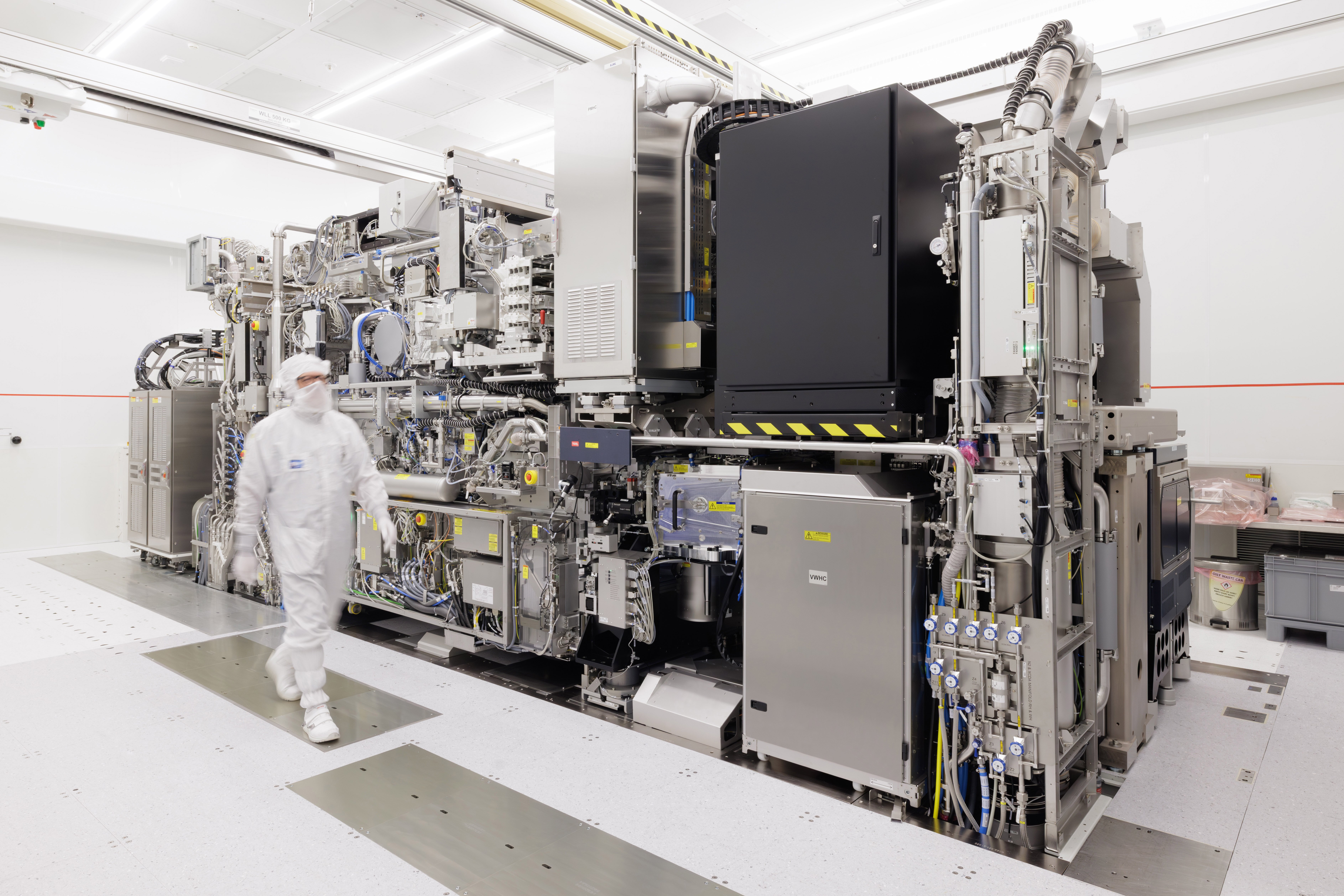 ASML TWINSCAN NXE:3800E EUV lithography system in a Veldhoven cleanroom, with a person in cleanroom clothing showing its scale.